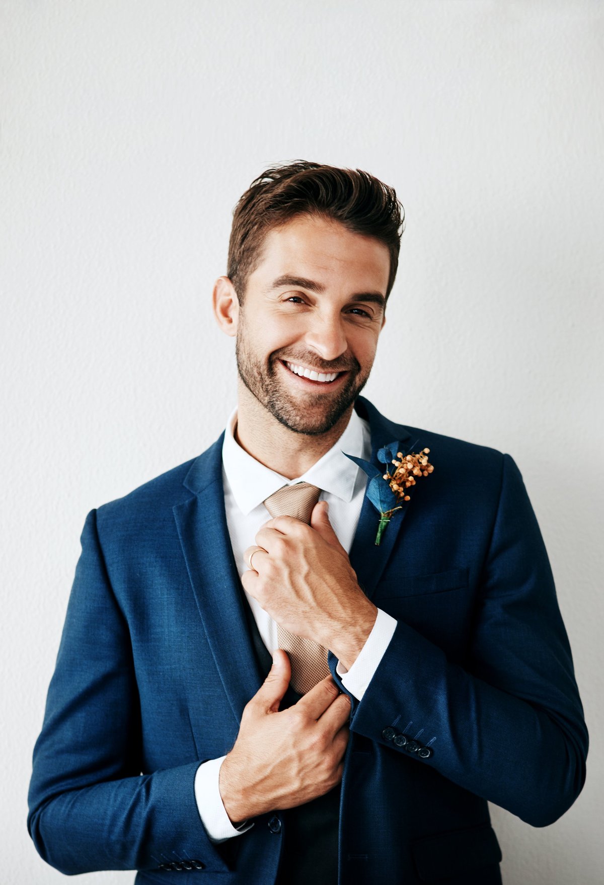 Studio portrait of handsome young groom in luxurious wedding suit against gray background