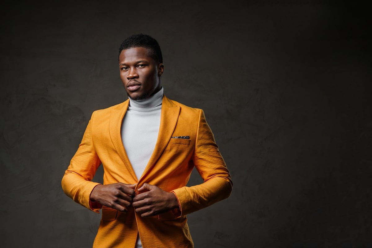 Stylish dark-skinned man posing in elegant yellow jacket against dark backdrop