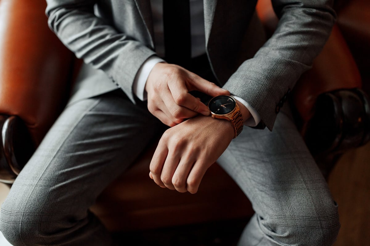 Man in suit sitting on chair looking at his luxury watch