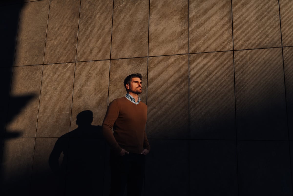 Businessman looking up in thought leaning against modern tiled wall