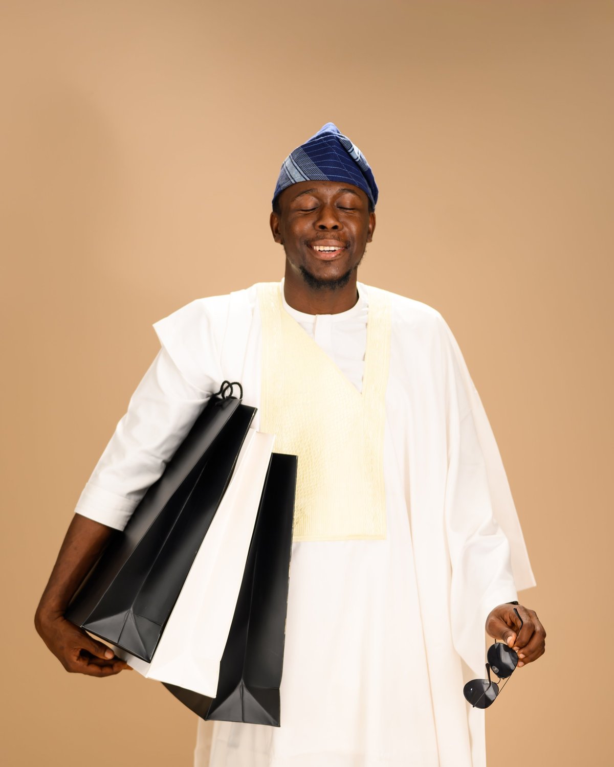 Young African man in white agbada with blue cap, smiling warmly
