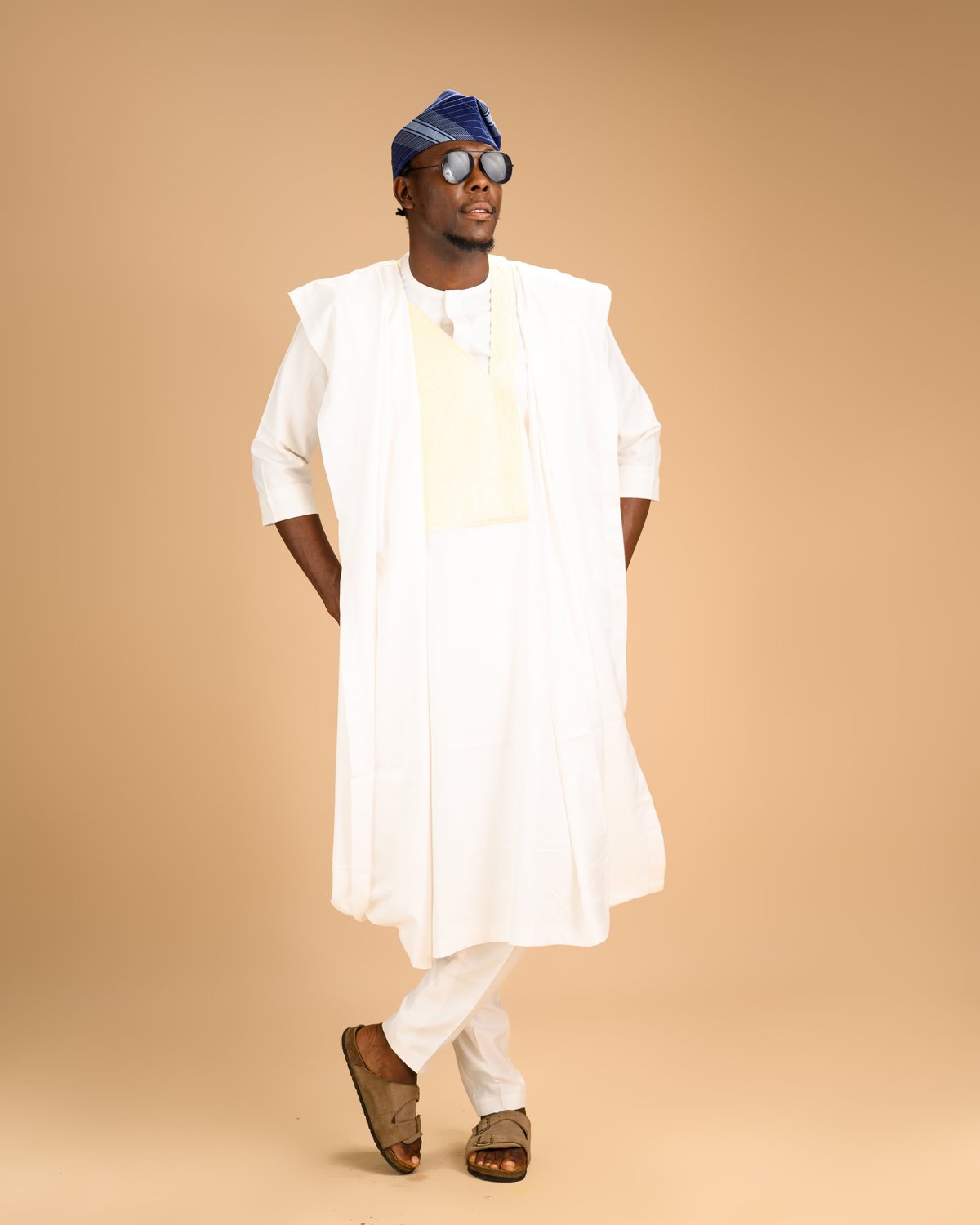 Full-length portrait of African man in white agbada with blue cap standing confidently