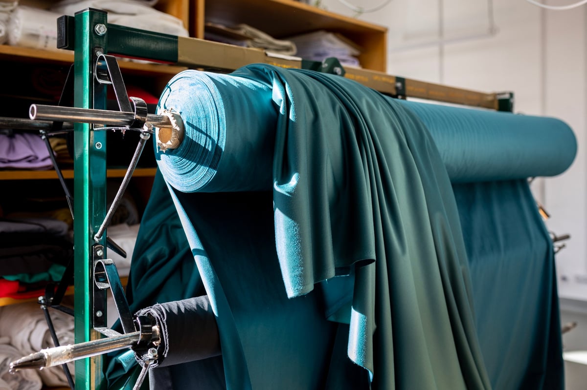 Large roll of teal-colored fabric on industrial rack in textile workshop
