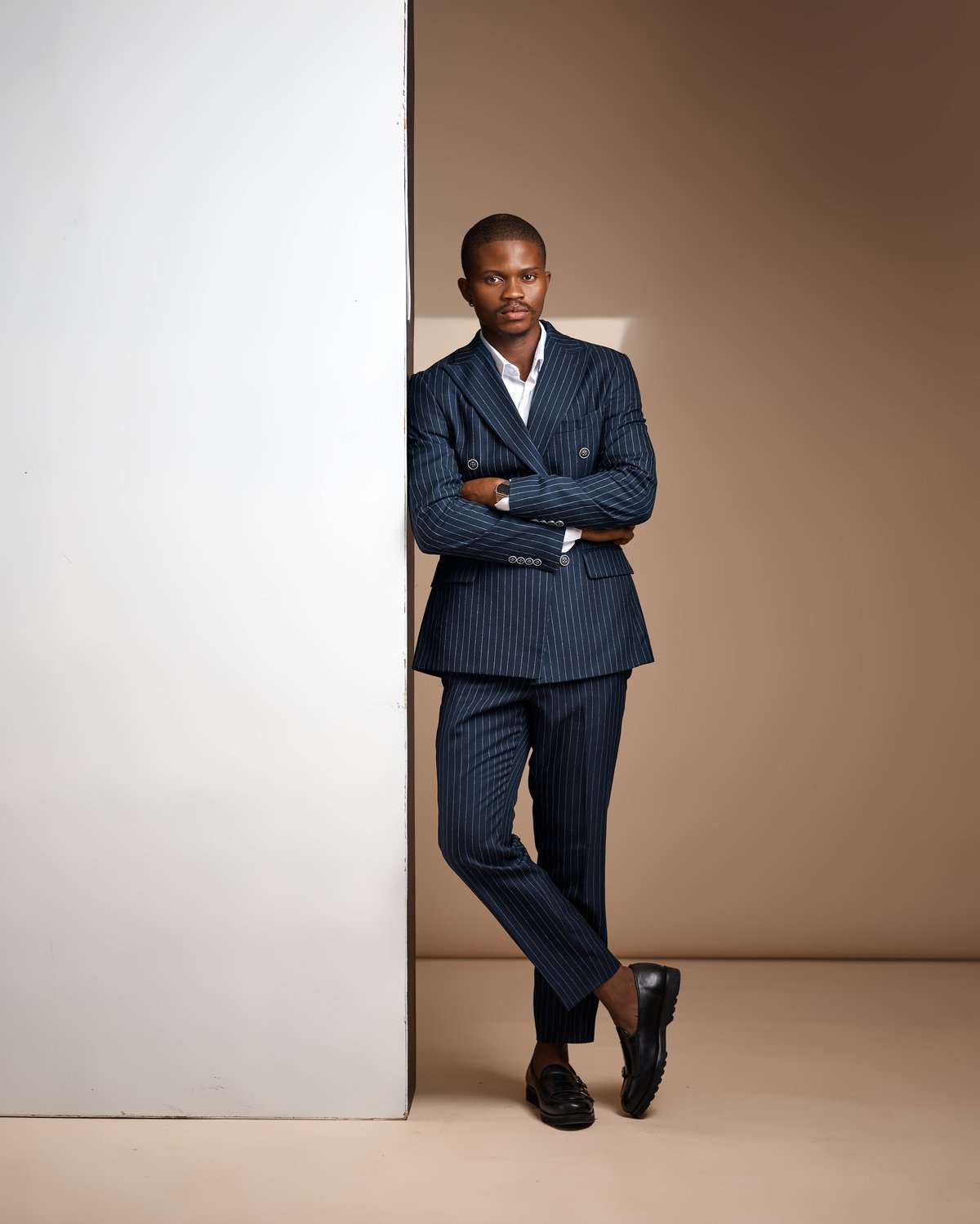 Elegant man in pinstripe suit leaning against panel in minimalist studio