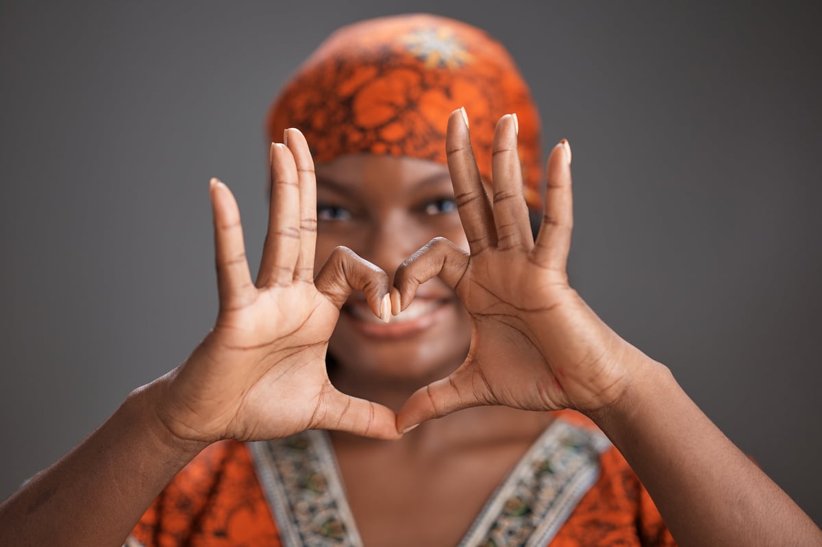 Woman in traditional clothing and headscarf forming heart shape with hands