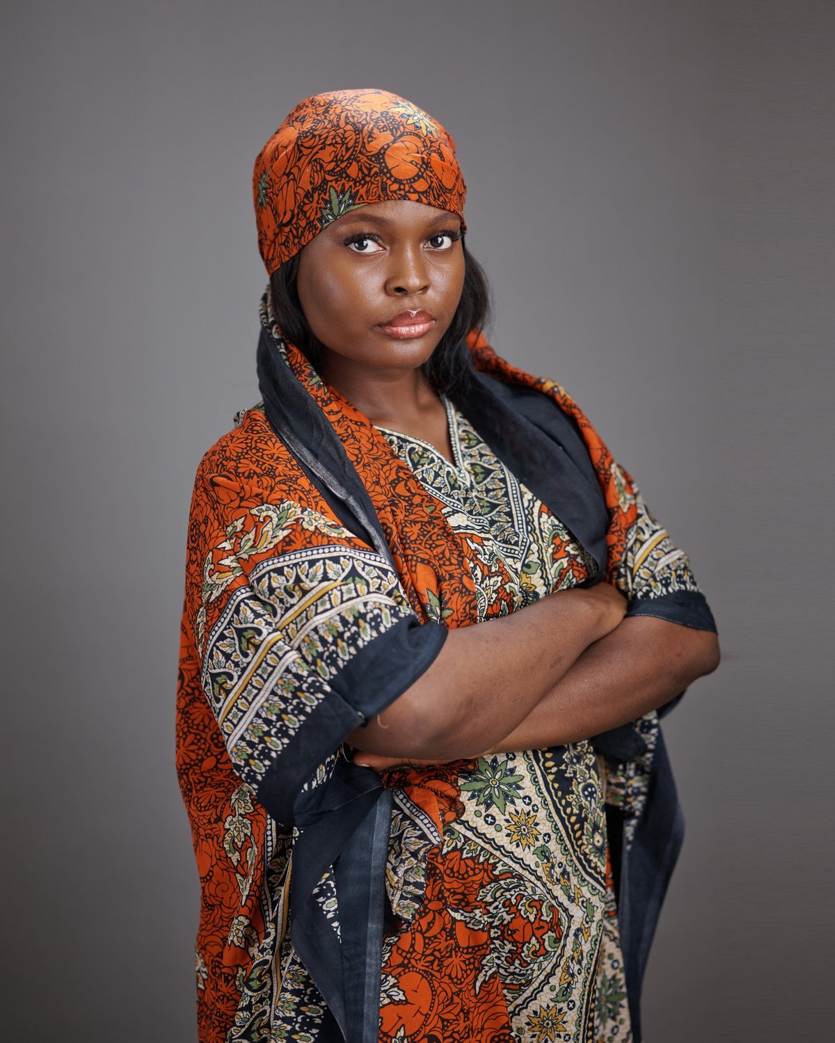 Young African woman in patterned traditional dress and matching headscarf arms crossed