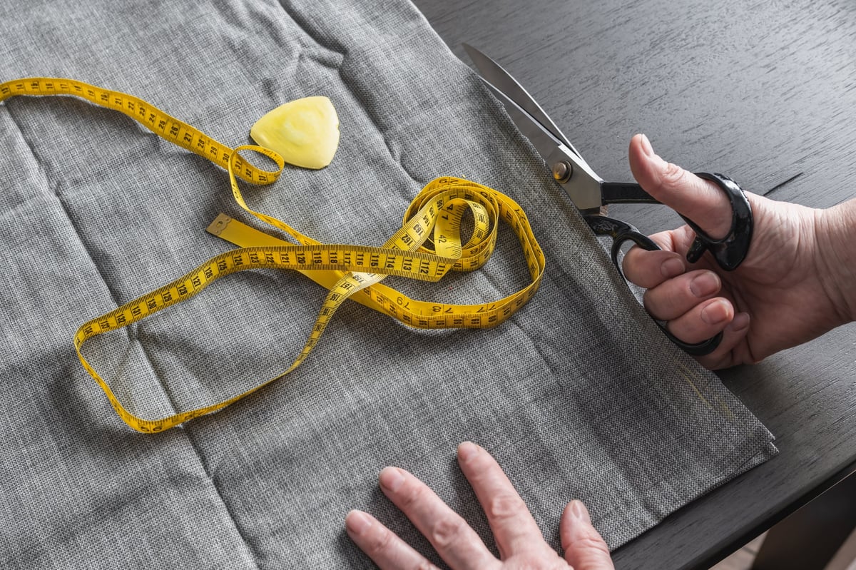 Hand cutting fabric with scissors. Yellow tape measure and tailor's chalk.