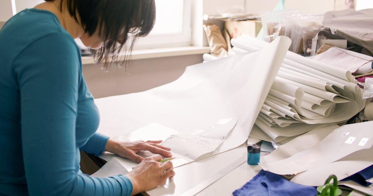 Dressmaking process with tailor creating garment patterns on table with paper drafts